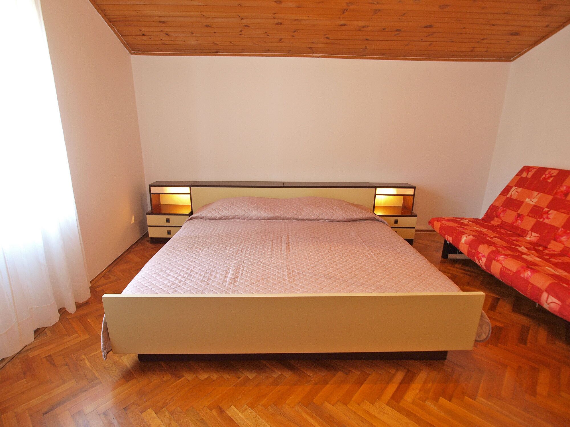 A bedroom with a bed, bedside tables, a chair, and a wooden ceiling.