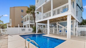 A pool area with a white fence, a lifeguard sign, and a multi-level building with balconies. - 5BR House with Private Pool Near Surfside Pier (Surfside Beach)