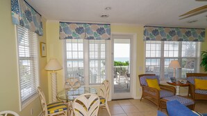 A living room with a glass table, wicker chairs, a blue sofa, and a view of the ocean through large windows. - 5BR House with Private Pool Near Surfside Pier (Surfside Beach)