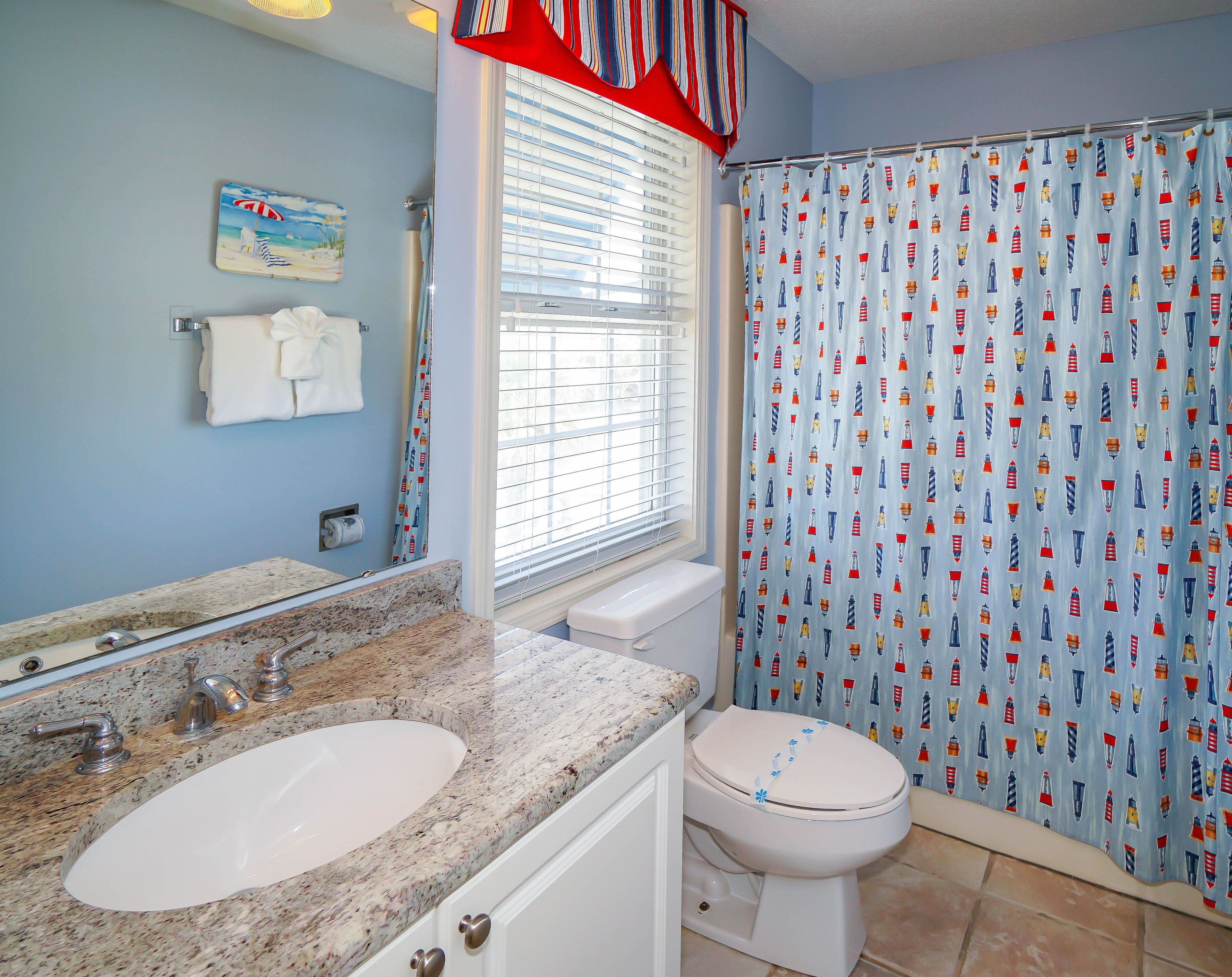 A bathroom with a granite countertop, a white sink, a toilet, and a shower curtain with maritime designs.