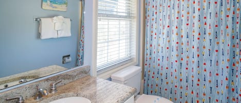 A bathroom with a granite countertop, a white sink, a toilet, and a shower curtain with maritime designs.