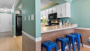 A kitchen with white cabinets, a black microwave, and blue bar stools. - Condo w/ Beach Walkover & Resort Pool Access (Surfside Beach)