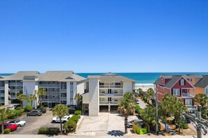 A beachfront hotel with multiple buildings, parking, and palm trees.