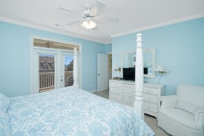 Une chambre à coucher comprenant un lit, une commode, une chaise, un ventilateur de plafond et une porte donnant sur un balcon.