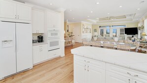 A spacious kitchen with white cabinetry, a large island, and a dining area with wicker chairs and a table. - Ocean View 6-Bedroom Beach Haven Sleeps 17 Near North Litchfield (North Litchfield)
