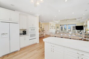 A spacious kitchen with white cabinetry, a large island, and a dining area with wicker chairs and a table.