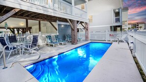Piscina com deck coberto, área de estar externa e cerca branca de piquete.