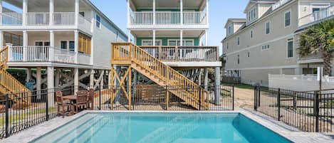 A swimming pool surrounded by multi-story buildings with balconies and a wooden staircase leading to a deck.