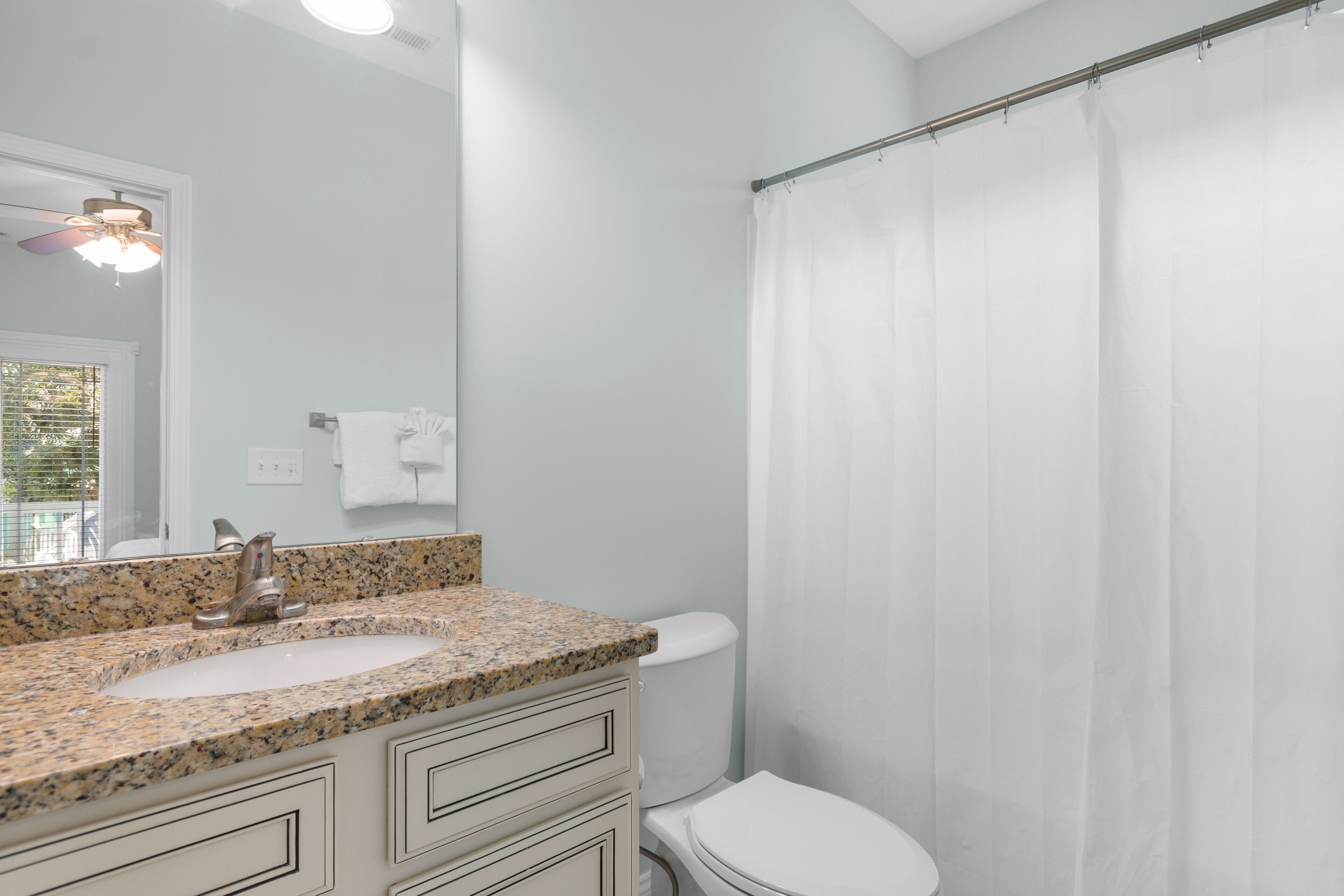A bathroom with a granite countertop sink, a white toilet, and a shower curtain.
