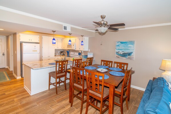 A compact kitchen with a central island, wooden dining table with chairs, and a ceiling fan. - Condo in Surfside Beach w/ Pool & Beach Access (Surfside Beach)
