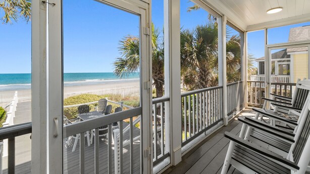 Une véranda couverte avec vue sur la plage, une terrasse en bois et du mobilier d’extérieur.