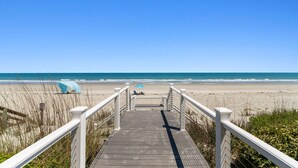 Une promenade en bois qui mène à une plage, avec un ciel dégagé.