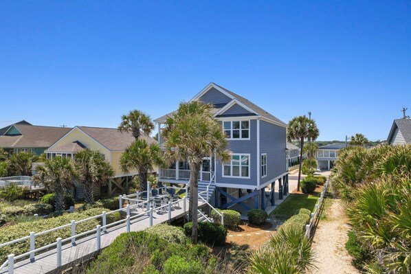 Una casa frente al mar con terraza, escaleras y vegetación circundante.