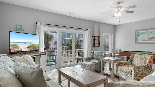 A living room with a large window, a pool table, and a television displaying a beach scene. - 5BR Ocean-Side Home w/ Private Pool & Ocean Views Near Surfside Pier (Surfside Beach)