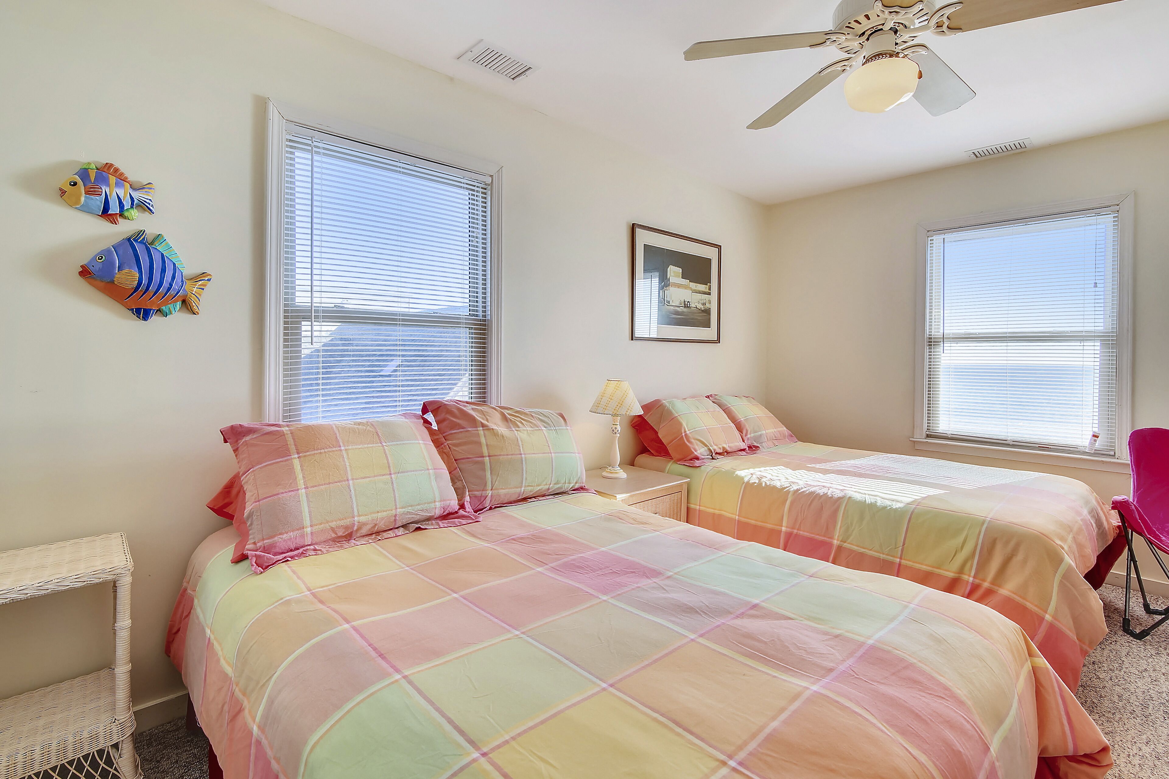 A bedroom with two beds, a ceiling fan, and a window with blinds.
