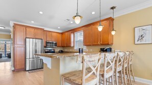 A modern kitchen with wooden cabinets, stainless steel appliances, and a central island with bar stools. - Walk to Beach 6BR Home w/ Private Pool & Ocean Views (Garden City Beach)