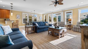 A spacious living room with a blue sofa, a coffee table, and a dining area with chairs. - Walk to Beach 6BR Home w/ Private Pool & Ocean Views (Garden City Beach)