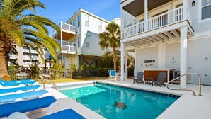 A swimming pool with blue lounge chairs, a palm tree, and a building with balconies. - Walk to Beach 6BR Home w/ Private Pool & Ocean Views (Garden City Beach)