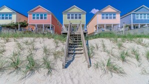 Une rangée de maisons de plage aux couleurs vives, avec un escalier en bois menant à la plage.