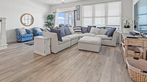 Un salon spacieux avec un grand canapé d’angle, un meuble blanc et un ventilateur de plafond.