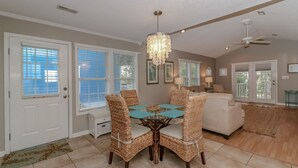 A dining area with a round table and four wicker chairs, a chandelier, and a ceiling fan.
