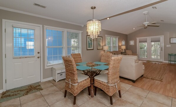 A dining area with a round table and four wicker chairs, a chandelier, and a ceiling fan. - Walk to Beach Villa Del Mar with Views & Private Porch (Surfside Beach)