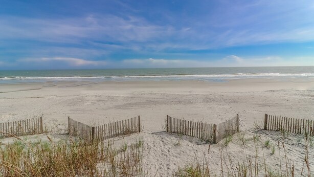 A sandy beach with a wooden fence and sparse vegetation in the foreground.