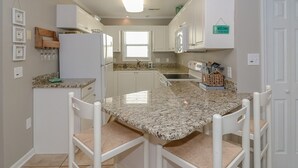 A kitchen with white cabinets, a granite countertop, and a dining area with white chairs.