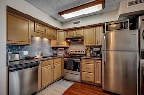 A compact kitchen with wooden cabinets, stainless steel appliances, and a built-in microwave. - Condo in Garden City Beach with Stunning Views & Beach Access (Garden City Beach)