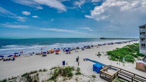 A beach with umbrellas, a pier, and a building with a balcony. - Condo in Garden City Beach with Stunning Views & Beach Access (Garden City Beach)