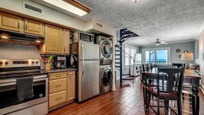 A kitchen with stainless steel appliances, wooden cabinets, and a dining area with a table and chairs. - Condo in Garden City Beach with Stunning Views & Beach Access (Garden City Beach)