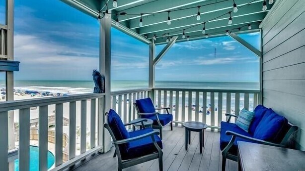A covered outdoor area with a view of the beach, featuring a pool, blue chairs, and a table. - Condo in Garden City Beach with Stunning Views & Beach Access (Garden City Beach)