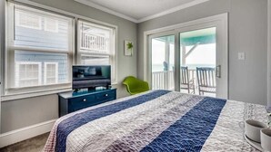 A bedroom with a bed, a TV, a desk, and a chair. There is a balcony with a view. - Condo in Garden City Beach with Stunning Views & Beach Access (Garden City Beach)