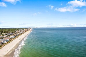 A coastal beach with buildings along the shore, a clear sky, and calm sea. - Walk to Beach: 5BR Surfside Beach Home w/ Private Pool (Surfside Beach)