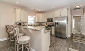 A kitchen with a central island, bar stools, a stainless steel refrigerator, and a microwave. - Haven: Walk to Surfside Beach & Pool in Pet-Friendly Home (Surfside Beach)