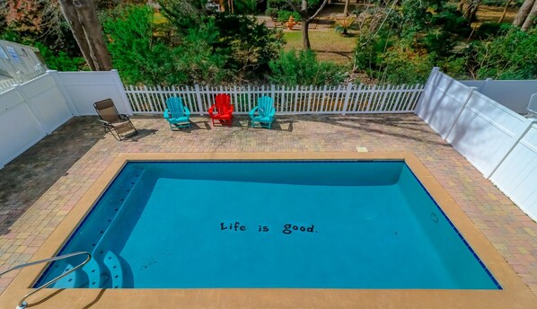 Una piscina rectangular con cerco blanco y sillas alrededor.