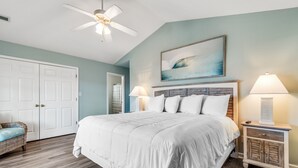 A bedroom with a large bed, a ceiling fan, a nightstand with a lamp, and a painting on the wall. - Walk to Beach Home w/ Private Pool & New Amenities for Families (Surfside Beach)