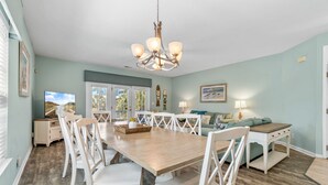 A dining area with a wooden table, white chairs, and a chandelier. - Walk to Beach Home w/ Private Pool & New Amenities for Families (Surfside Beach)