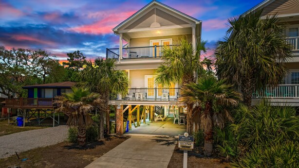 A multi-story hotel with a balcony on the second floor, surrounded by palm trees and a pathway leading to the entrance. - Walk to Beach Home w/ Private Pool & New Amenities for Families (Surfside Beach)