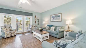 A living room with a ceiling fan, a light-colored sofa, a coffee table, and a window with blinds. - Walk to Beach Home w/ Private Pool & New Amenities for Families (Surfside Beach)