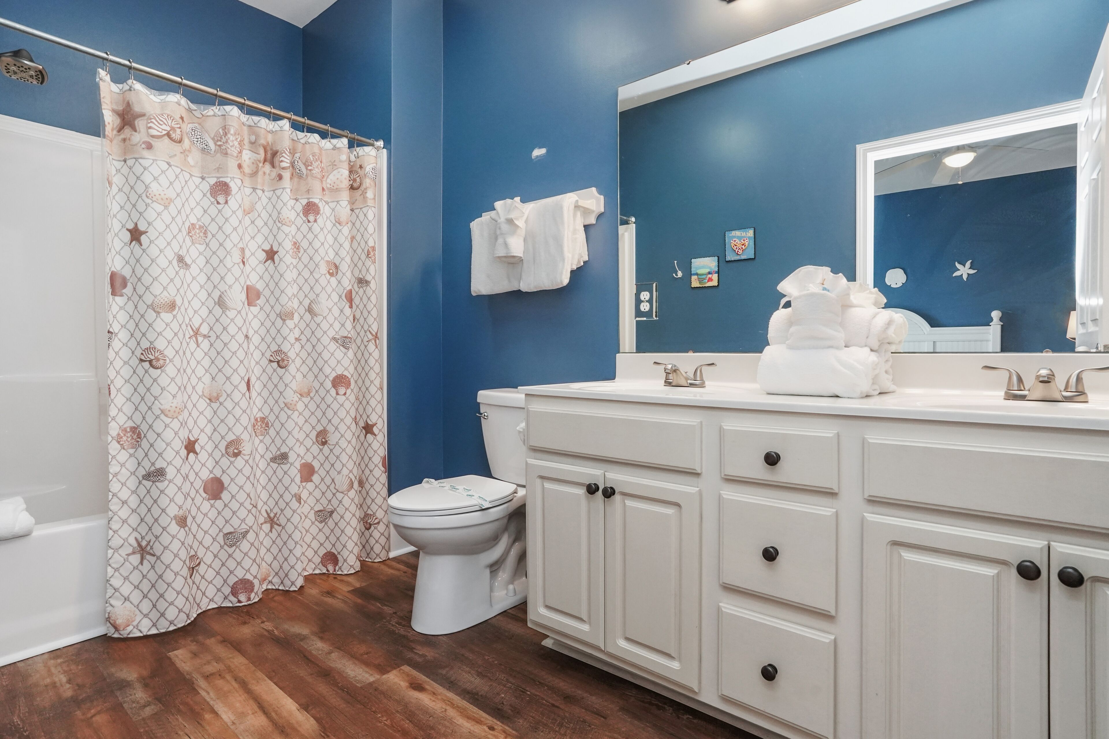 A bathroom with a blue wall, white vanity, and a shower curtain with a shell pattern.