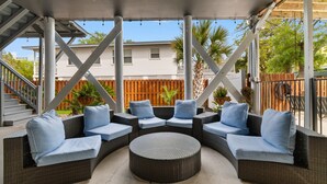 Eine Terrasse im Freien mit Korbmöbeln, einem runden Tisch und einem Holzzaun im Hintergrund.