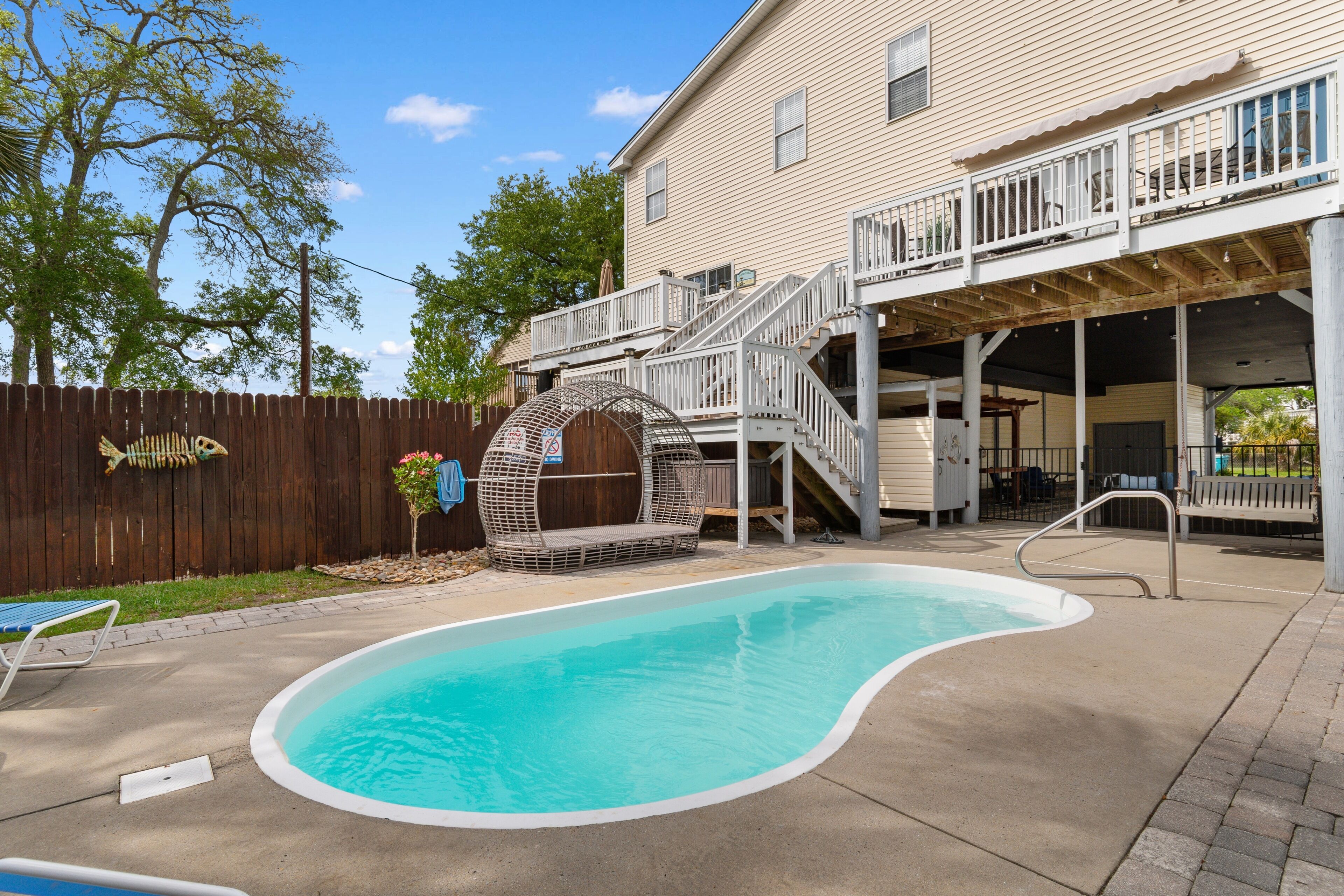 Un patio trasero con piscina, terraza de madera y una casa con balcón.