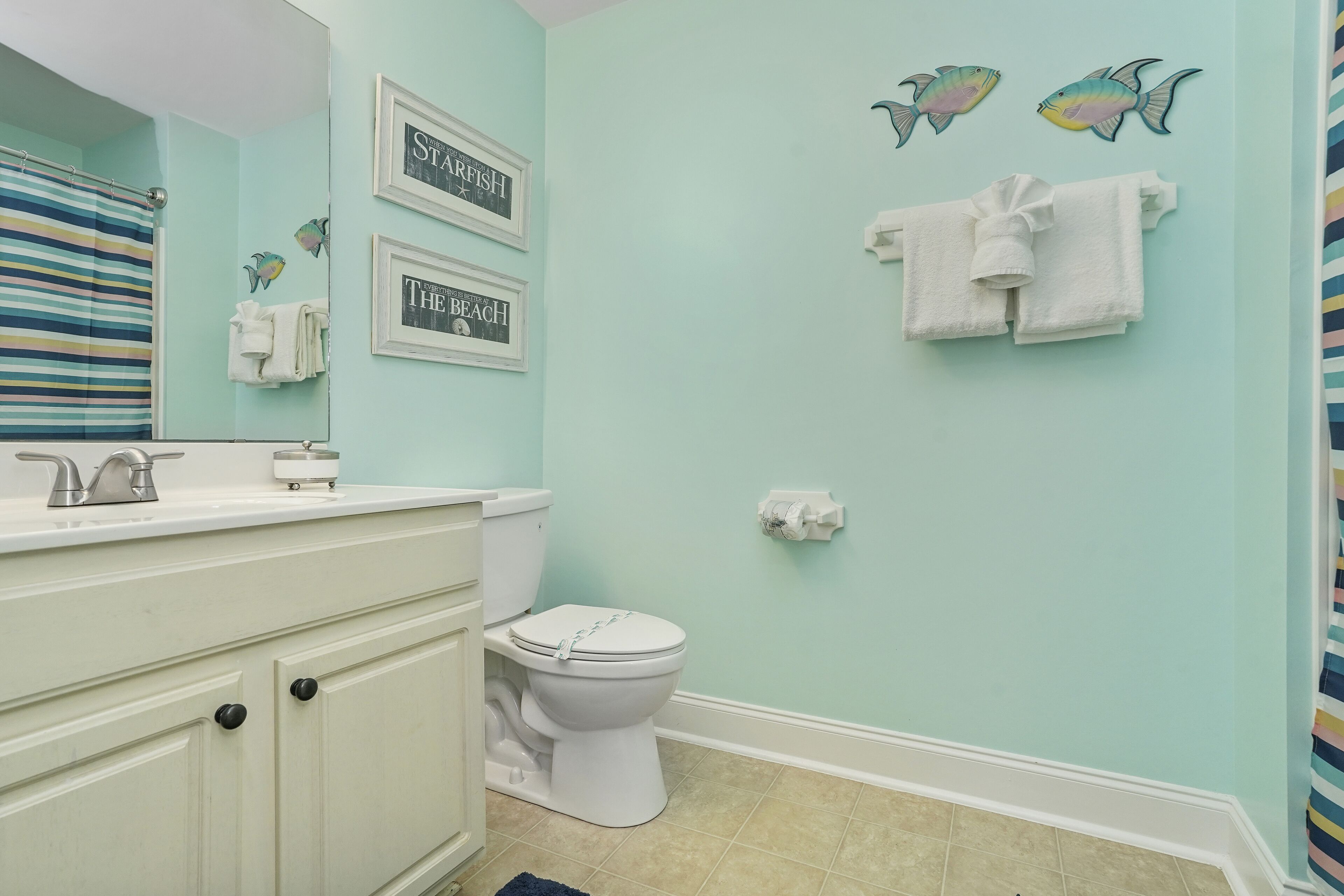 A bathroom with a white toilet, a white sink, and a striped shower curtain. There are framed pictures on the wall and a towel rack with white towels.