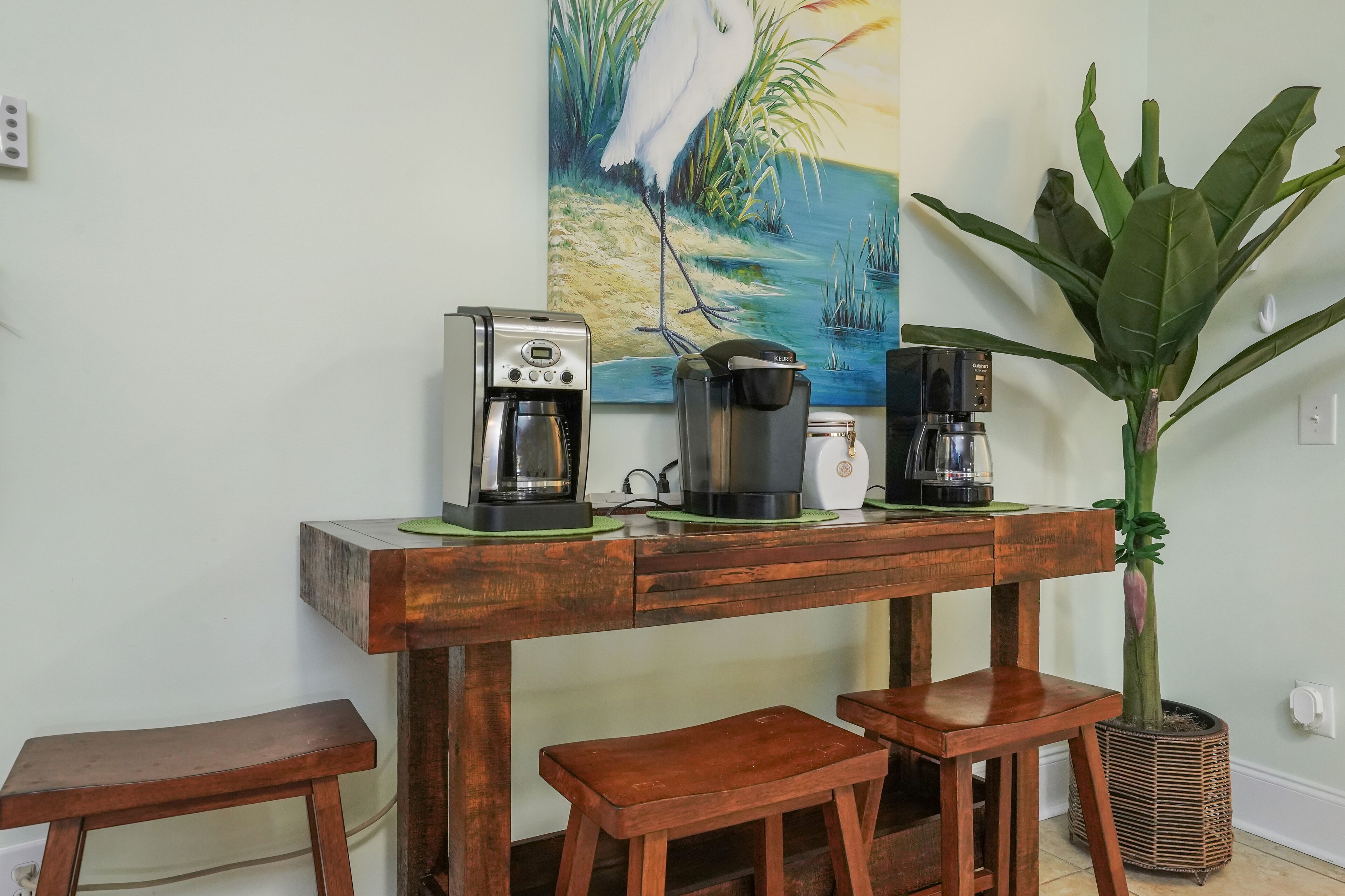 Une table en bois, avec deux machines à café et une grande plante.