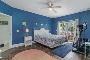 A bedroom with a bed, a ceiling fan, a treadmill, and a window with a view of the outside.