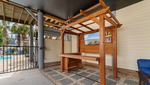 Ein überdachter Patio-Bereich mit einer Holzhütte, einem Pool und Blick auf Palmen und Häuser.