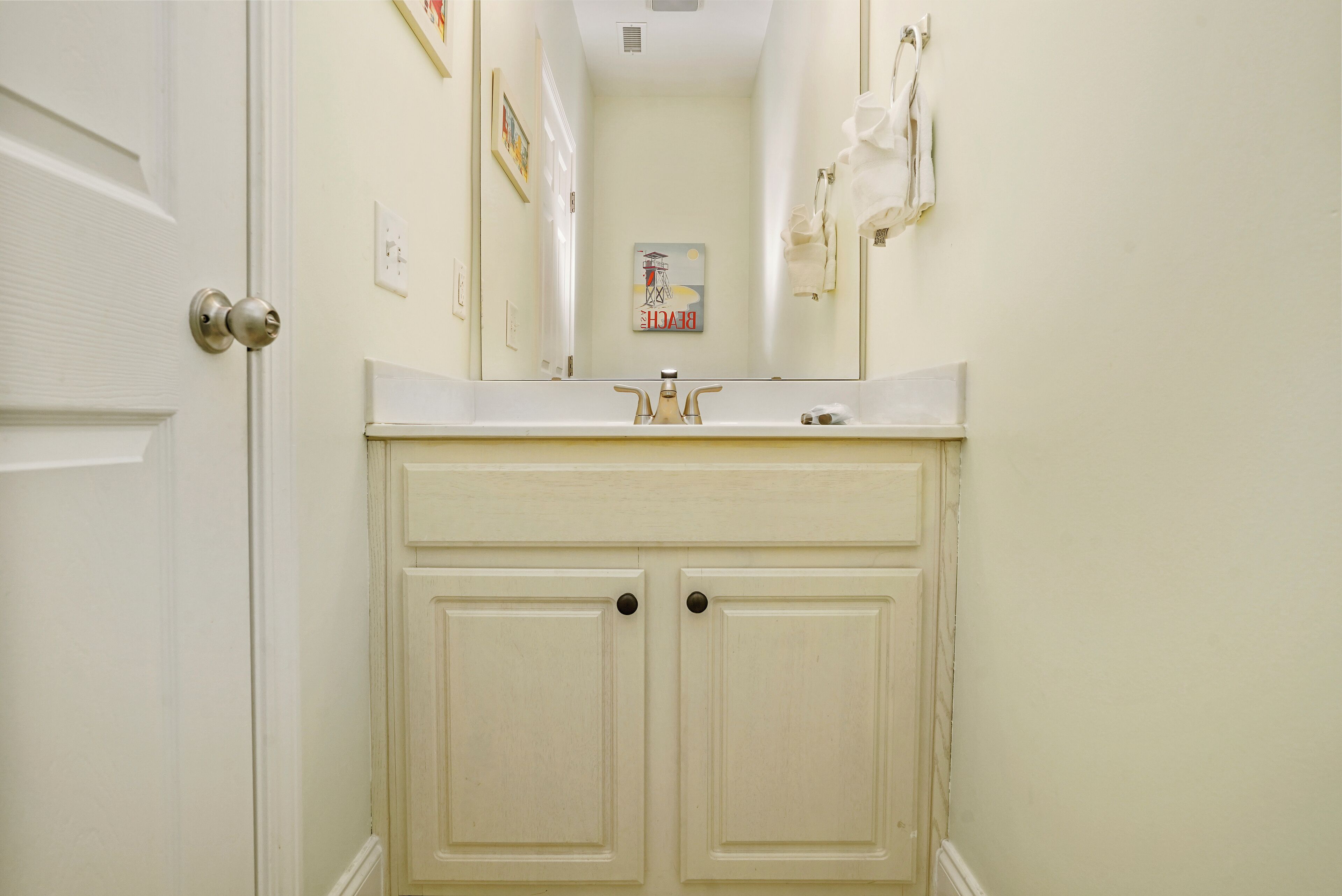 A narrow hallway with a white door, a white sink with a mirror above it, and a towel rack on the wall.