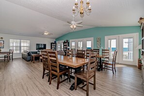 A spacious living room with a wooden dining table, chairs, a sofa, and a TV. There are bookshelves, a chandelier, and a ceiling fan. - Pier Pressure: Second Row Home, Walk to Pier, 7BR (Garden City Beach)