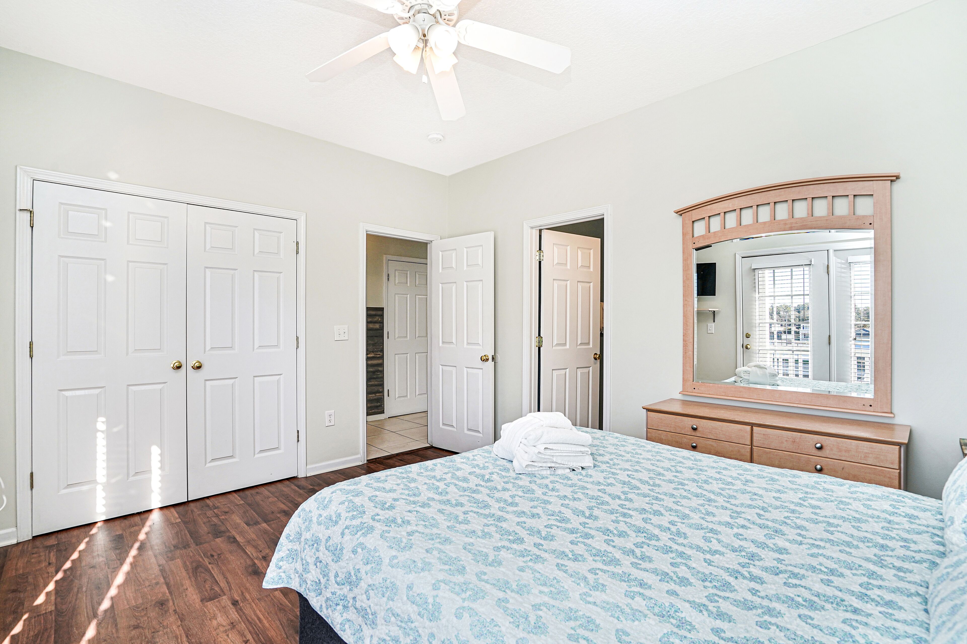 A bedroom with a bed, a dresser, a mirror, and a ceiling fan.